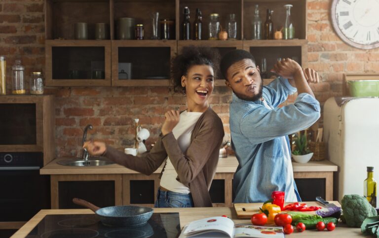 Black couple dancing near table with food in kitchen
