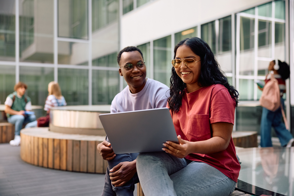 Happy Indian student and her male friend using laptop and university campus.